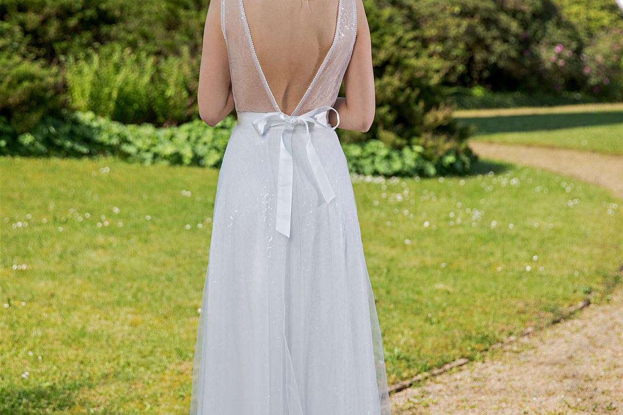 Eine junge Frau in einem weißen, fließenden Kleid steht auf einem Pfad vor einem historischen Gebäude.