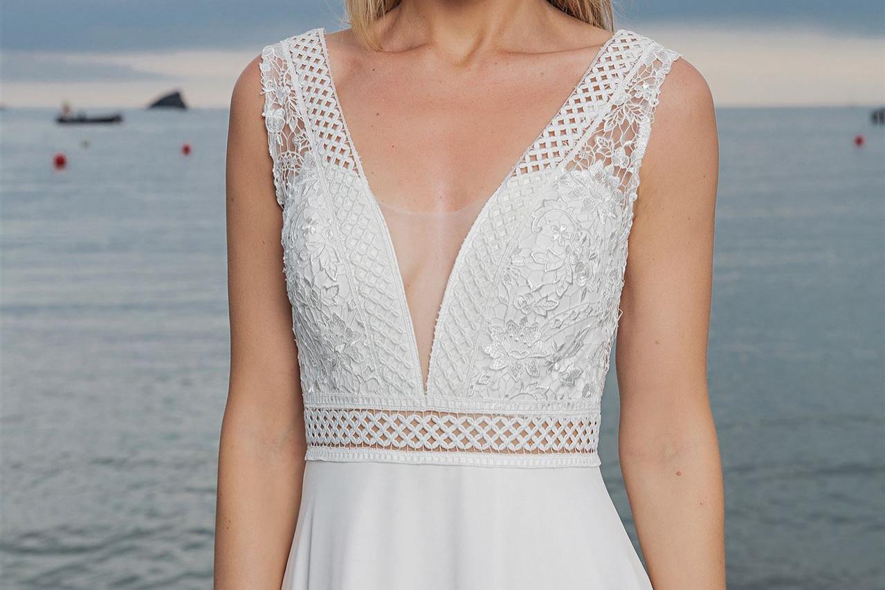 Eine blonde Frau in einem weißen Spitzenkleid vor einer weiten Wasserkulisse.