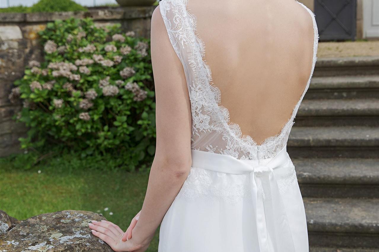 Eine blonde Frau in einem weißen Kleid blickt über ihre Schulter, während sie an einem steinernen Geländer lehnt.