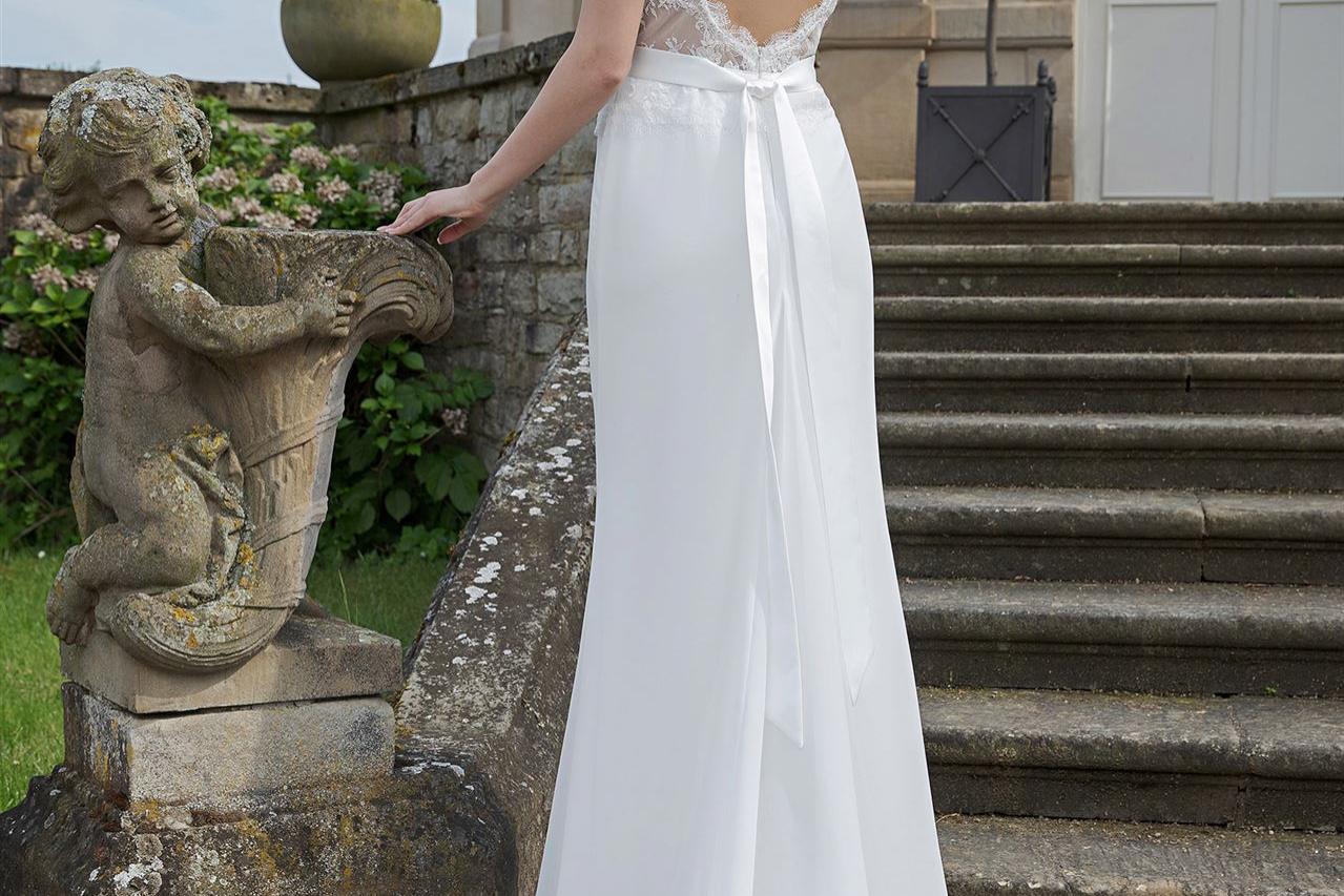 Eine blonde Frau in einem weißen Hochzeitskleid posiert vor einer steinernen Treppe und einem klassizistischen Gebäude.