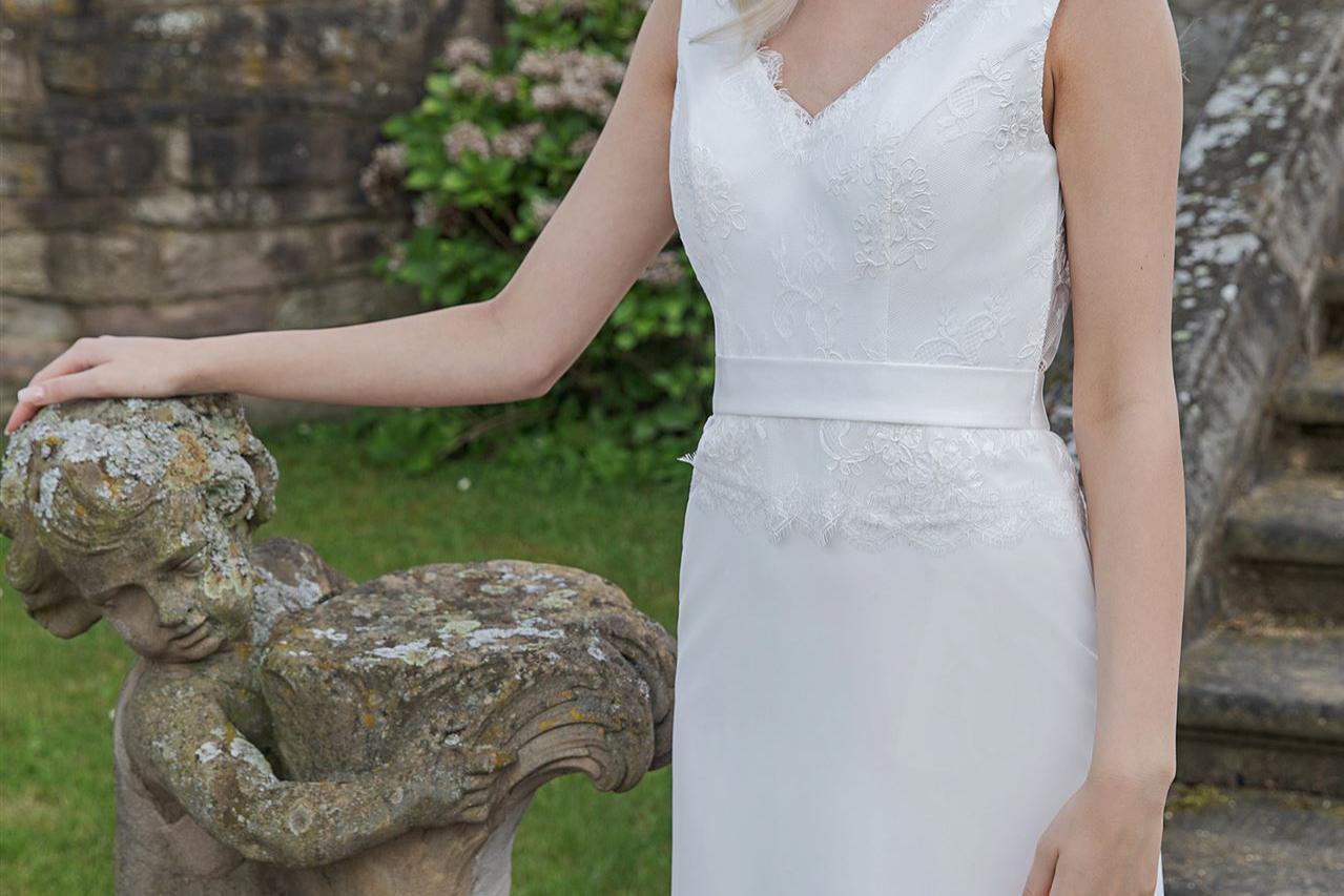 Blonde Frau in einem weißen Hochzeitskleid vor einer antiken Steinstatue an einer historischen Fassade.