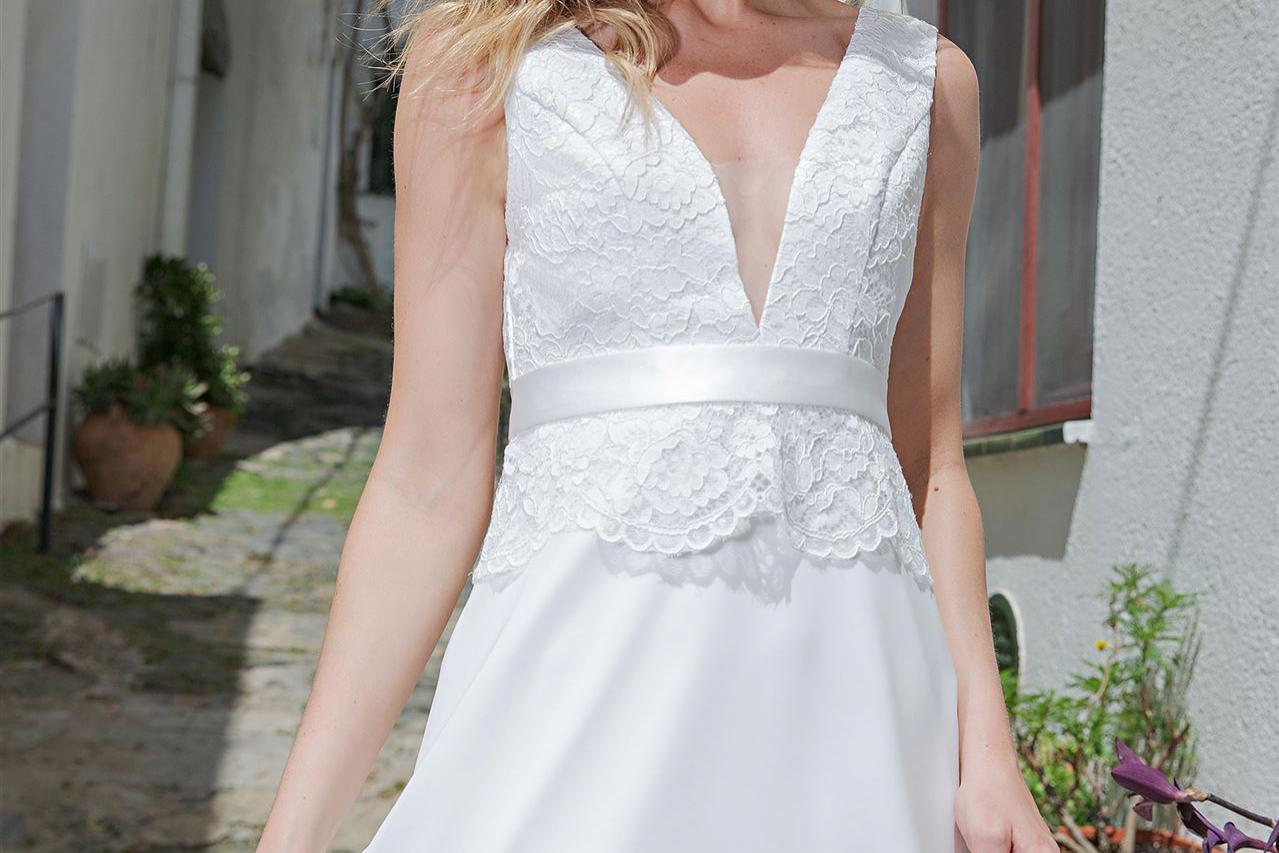 Eine blonde Frau in einem weißen, eleganten Kleid steht in einem historischen Außenbereich.