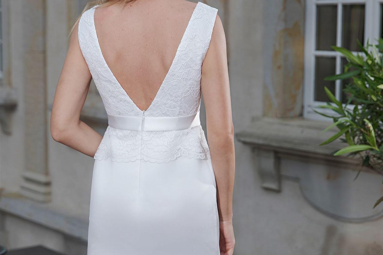 Blonde Frau in einem weißen Kleid wird von der Seite in einem historischen Innenhof aufgenommen.
