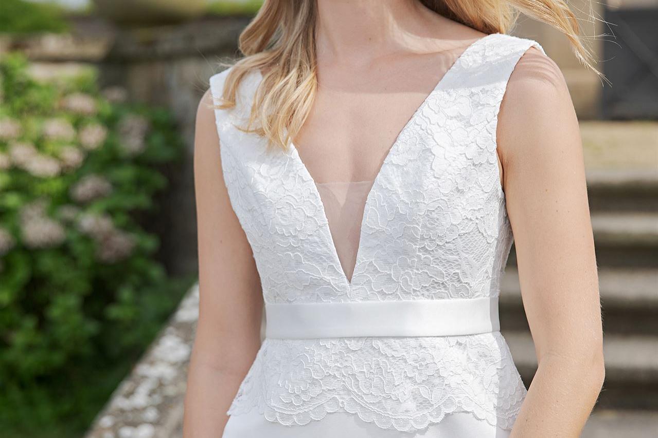 Eine blonde Frau in einem eleganten, weißen Kleid posiert im Freien vor einer steinernen Treppe.