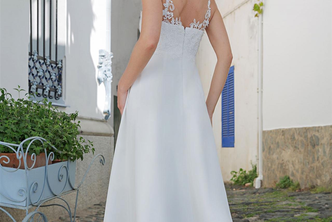 Eine Frau in einem langen, weißen Brautkleid steht in einer hellen, mediterranen Gasse.