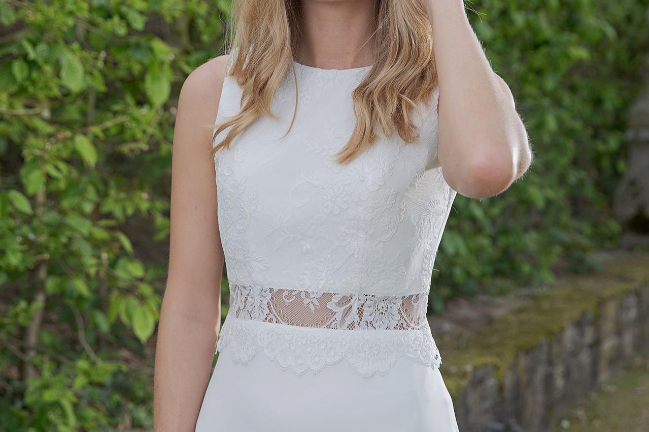 Eine blonde Frau in einem weißen Kleid inmitten einer üppigen grünen Gartenlandschaft.