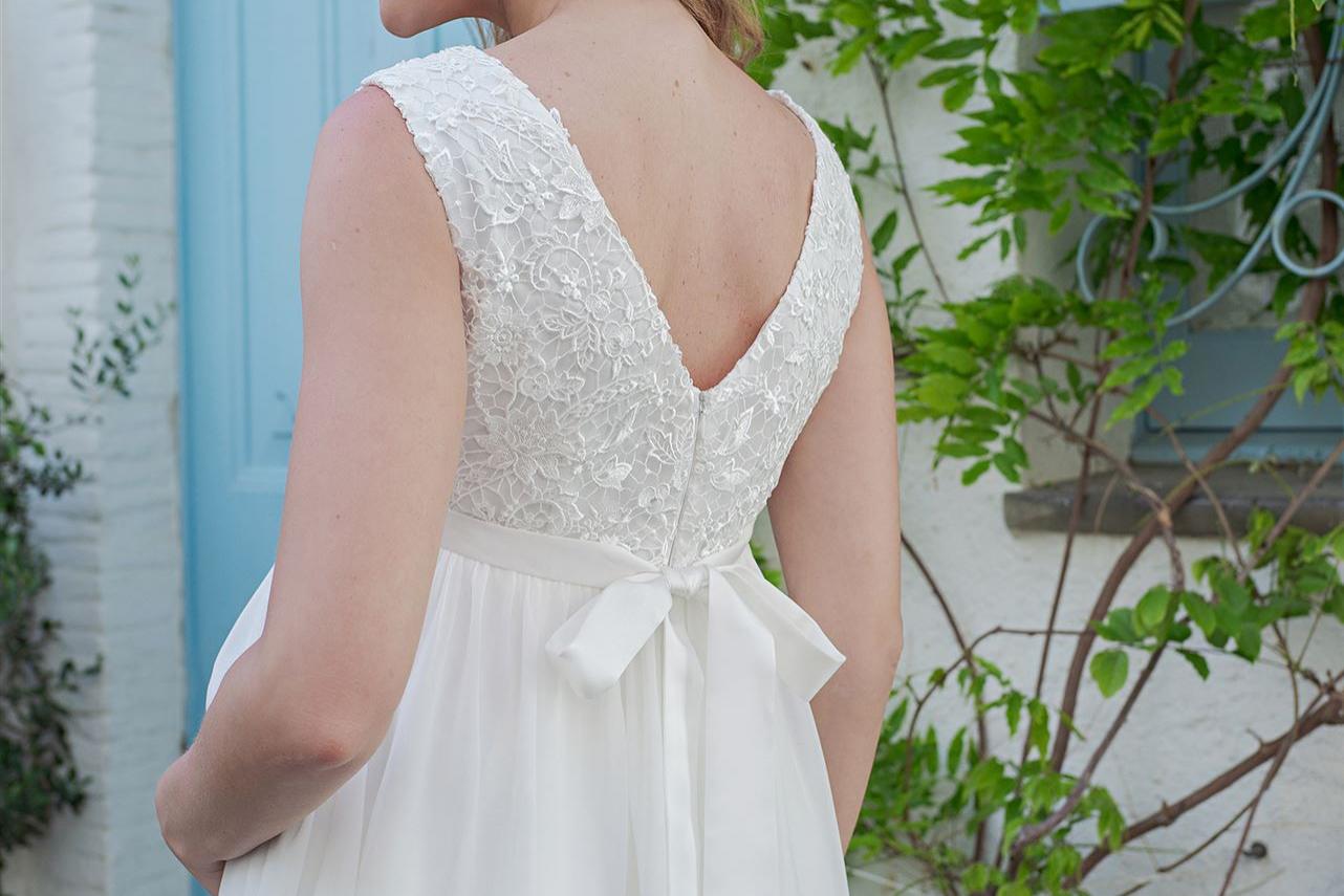 Eine junge Frau in einem weißen Brautkleid mit Spitzendetail vor einer grünen Fassade.