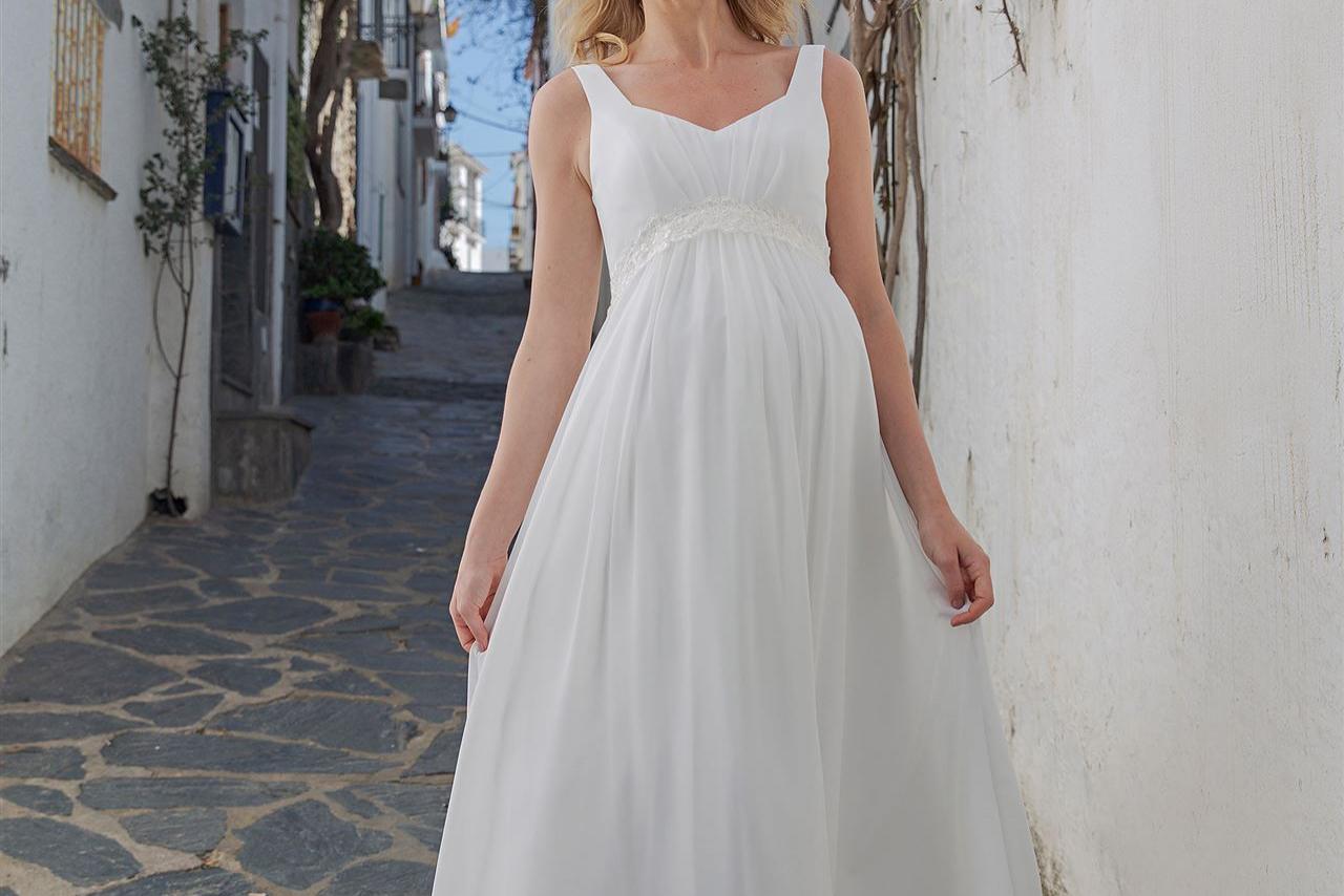 Blonde Frau in weißem Kleid in einer engen Gasse mit roten Blumen
