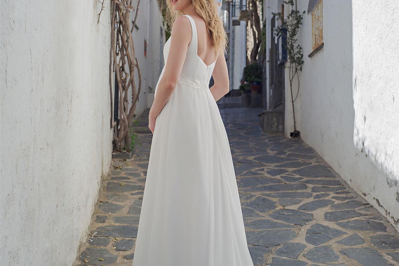 Eine blonde Braut in einem weißen Kleid steht in einem schmalen, historischen Gassenweg.