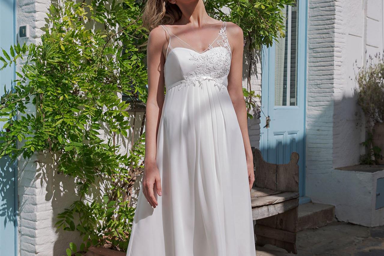 Eine Frau in einem weißen Kleid steht vor einer von dichtem Grün überwucherten Hausfassade.