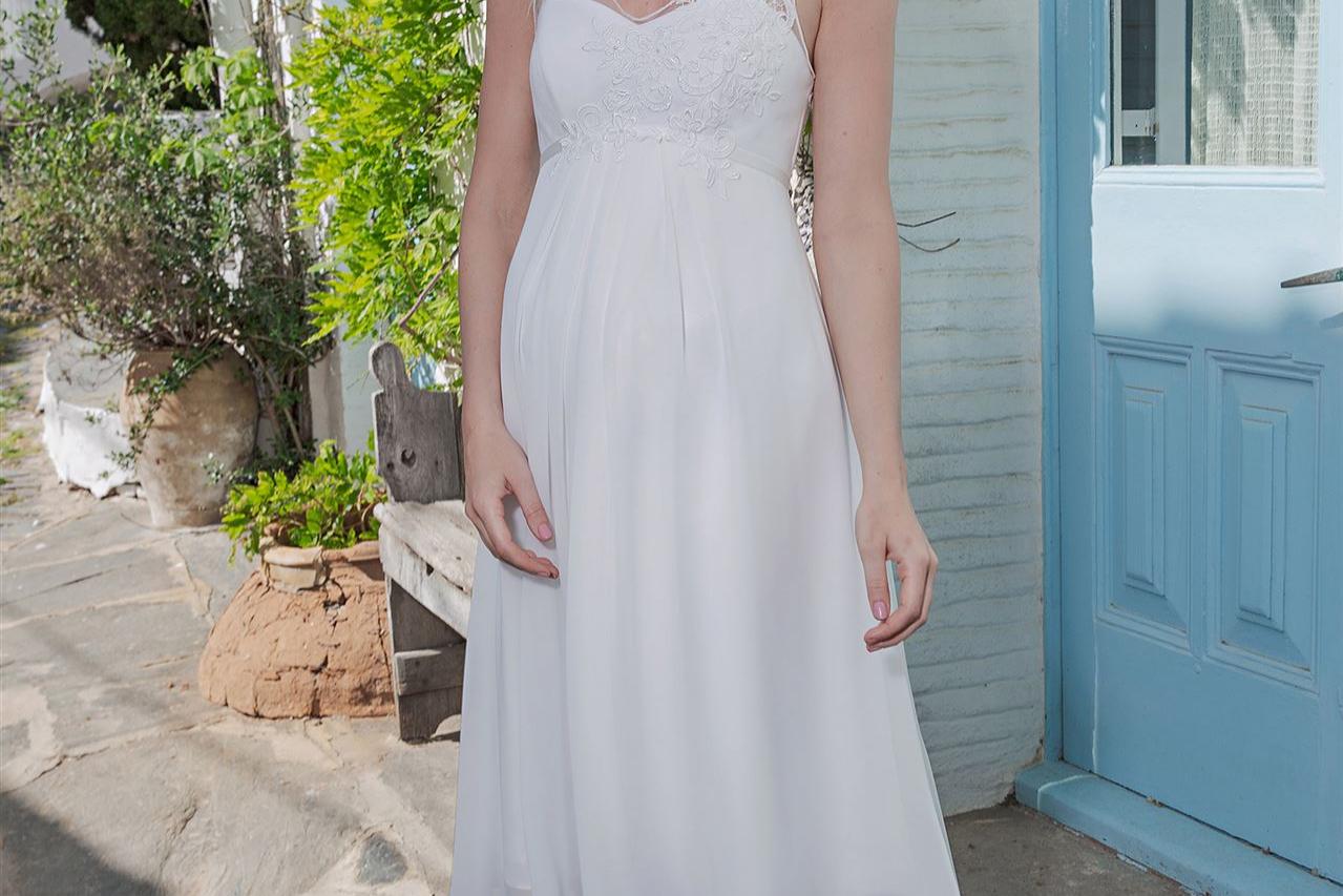 Eine junge Frau in einem fließenden hellen Sommerkleid vor einer grünen Fassade.
