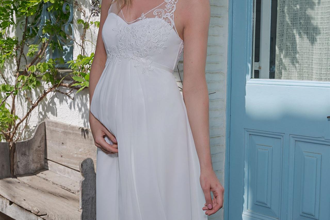 Blonde Frau in weißem Sommerkleid vor einer hellblauen Tür und üppigem Grün.