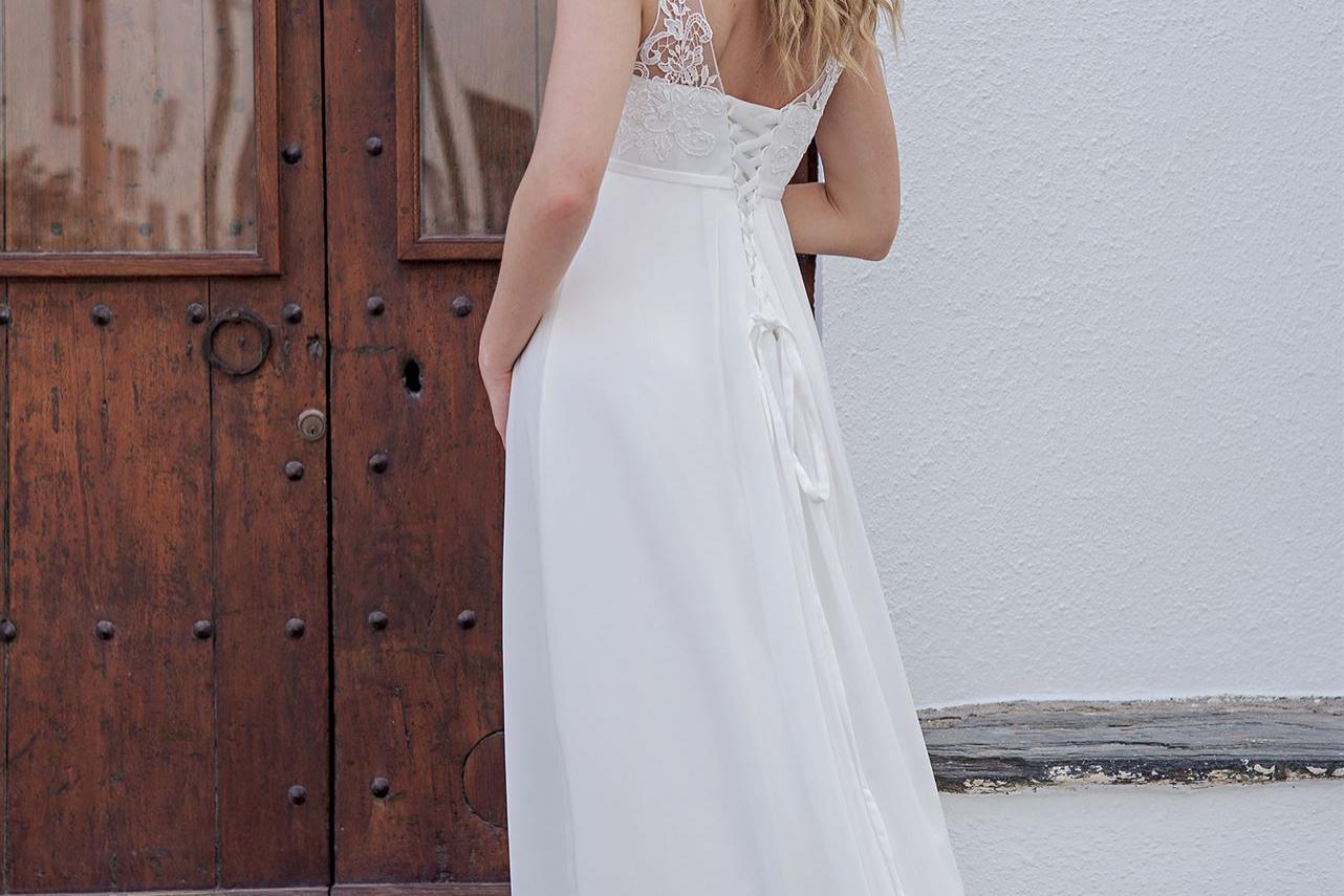 Eine Frau in einem fließenden weißen Kleid steht vor einer großen, rustikalen Holztür.