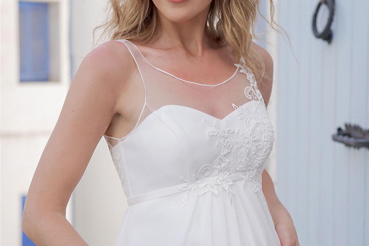 Eine schwangere Frau in einem weißen Kleid steht vor einer hellen, modernen Architekturfassade.